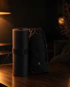 Deep Delta Field Mat rolled beside its carry bag on a walnut surface at night